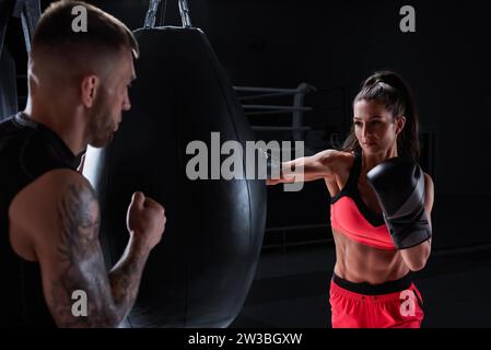 Sportliche Frau in roten Shorts und Oberteil boxt mit einem Trainer. Boxen und Mixed Martial Arts Konzept. Gemischte Medien Stockfoto