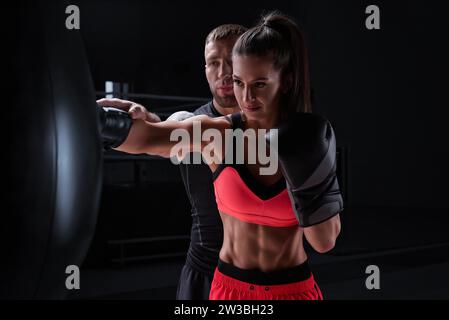 Sportliche Frau in roten Shorts und Oberteil boxt mit einem Trainer. Boxen und Mixed Martial Arts Konzept. Gemischte Medien Stockfoto