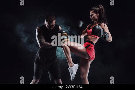 Sportliche Frau in roten Shorts und Oberteil boxt mit einem Trainer. Boxen und Mixed Martial Arts Konzept. Gemischte Medien Stockfoto