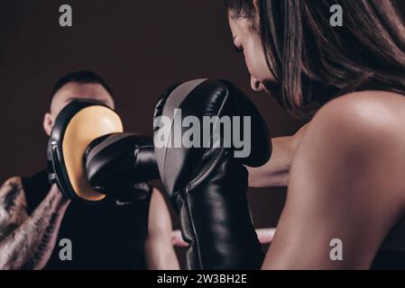 Sportliche Frau in roten Shorts und Oberteil boxt mit einem Trainer. Boxen und Mixed Martial Arts Konzept. Gemischte Medien Stockfoto