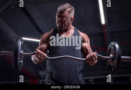 Bild eines starken Athleten, der eine Langhantel in einem Fitnessstudio hebt. Bizepspumpen. Fitness- und Bodybuilding-Konzept Stockfoto