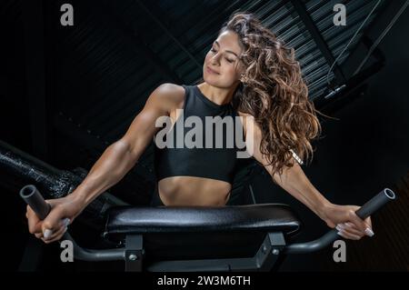 Charmante Brünette, die Hyperextension im Fitnessstudio macht. Drücken Sie die Pumpe. Fitness- und Bodybuilding-Konzept. Gemischte Medien Stockfoto