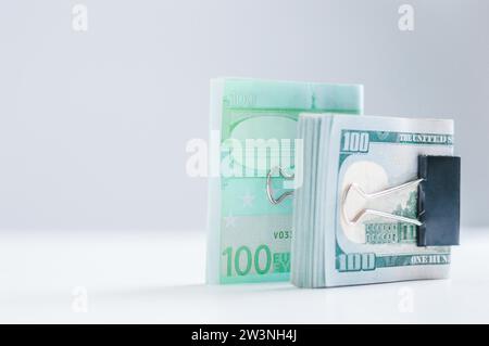 Päckchen mit Euro und Hundert-Dollar-Scheinen liegen auf einem weißen Tisch, der mit Büroklammern verschlossen ist. Das Konzept der Einsparungen während der Krise. Dollar vs. Euro. Stockfoto