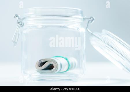 Eine Packung mit 100-Dollar-Scheinen liegt in einem Glas. Das Konzept der Einsparungen während der Krise. Gemischte Medien Stockfoto