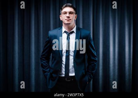 Ein erwachsener Mann steht in einem Anzug vor einem schwarzen Vorhang. Geschäftskonzept. Das Verwaltungspersonal des Unternehmens. Gemischte Medien Stockfoto