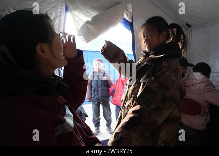 (231221) -- LINXIA, 21. Dezember 2023 (Xinhua) -- Ein Experte für psychische Gesundheit eines psychologischen Beratungsteams kommuniziert mit einem Kind an einem vorübergehenden Umzugsort im Dorf Yangwa im Bezirk Jishishan, nordwestchinesische Provinz Gansu, 21. Dezember 2023. Nach dem Erdbeben der Stärke 6,2 in der Provinz Gansu im Nordwesten Chinas sind insgesamt 28 Experten für psychische Gesundheit auf nationaler und provinzieller Ebene nach Gansu gekommen, um stationäre Patienten und deren Gefährten, die Familien der Opfer und diejenigen, die vom Erdbeben betroffen sind, einschließlich der Katastrophenhelfer, psychologische Beratung anzubieten. Gansu i Stockfoto