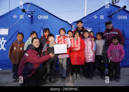 (231221) -- LINXIA, 21. Dezember 2023 (Xinhua) -- Kinder posieren für ein Foto mit Mitgliedern eines psychologischen Beratungsteams nach einem Gruppenmalkurs an einem temporären Umzugsort im Dorf Yangwa im Jishishan County, nordwestchinesische Provinz Gansu, 21. Dezember 2023. Nach dem Erdbeben der Stärke 6,2 in der Provinz Gansu im Nordwesten Chinas sind insgesamt 28 Experten für psychische Gesundheit auf nationaler und provinzieller Ebene nach Gansu gekommen, um stationäre Patienten und deren Gefährten, die Familien der Opfer und die vom Erdbeben betroffenen Personen, einschließlich Katastrophenhilfe, psychologische Beratung anzubieten Stockfoto
