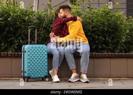 Fernbeziehung. Wunderschönes Paar, das sich draußen auf Bank und Koffer umarmt Stockfoto