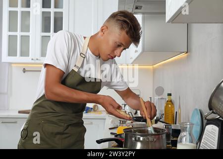 Mann, der geriebenen Käse in einen Topf in einer unordentlichen Küche steckt. Viele schmutzige Geschirr und Utensilien auf der Arbeitsplatte Stockfoto