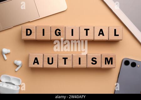 Phrase Digital Autismus aus Holzwürfeln und Geräten auf beigefarbenem Hintergrund, flache Lage. Suchtverhalten Stockfoto