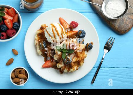 Köstliche belgische Waffeln mit Eis, Beeren und Karamellsauce serviert auf hellblauem Holztisch, flach gelegt Stockfoto