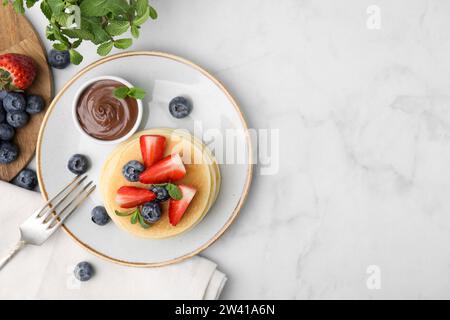 Köstliche Pfannkuchen mit Erdbeeren, Heidelbeeren, Minze und Schokoladensauce auf hellem Marmortisch, flach gelegt. Leerzeichen für Text Stockfoto