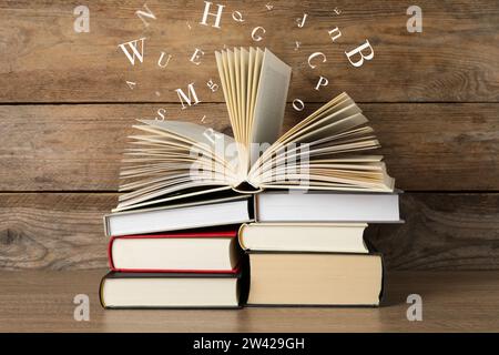 Offenes Buch mit Buchstaben, die auf hölzernem Hintergrund herausfliegen Stockfoto