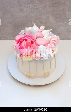 Schöner und eleganter Kuchen, dekoriert mit geschmolzener grauer Schokolade, Makronen, essbarer rosa Pfingstrosenblüte, Schokoladenbissen und Baisons Stockfoto