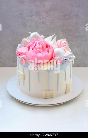 Schöner und eleganter Kuchen, dekoriert mit geschmolzener grauer Schokolade, Makronen, essbarer rosa Pfingstrosenblüte, Schokoladenbissen und Baisons Stockfoto