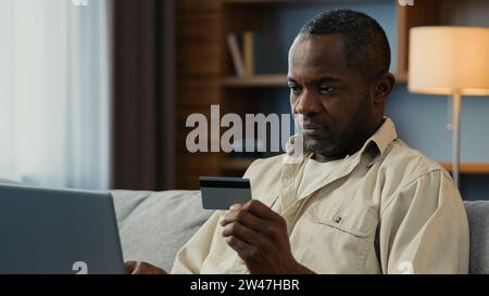 Lächelnder afroamerikanischer Mann männlicher Kunde machen Kreditkartenzahlung online Laptop Remote Pay Kauf mit sofortiger sicherer Transaktion von Stockfoto