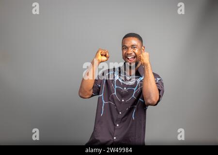 Überregter junger Schwarzer, der die Faust auf weißem Hintergrund hochhebt und den Erfolg feiert. Glücklicher afrikanischer Millennial-Mann, der positive Emotionen teilt, Copy Spa Stockfoto