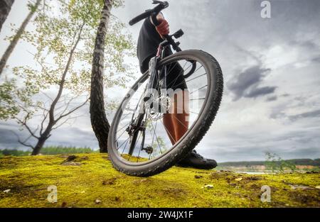 Radfahrer stehen mit einem Fahrrad auf einem moosbewachsenen Felsen. Flachwinkelansicht. Sport und Outdoor-Reisen. Stockfoto