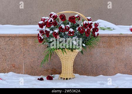 Korb mit roten Rosen bedeckt mit Schnee steht an der Gedenkstätte im Winter Stockfoto