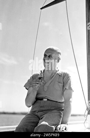 Mr. Hagedoorn lächelt mit einem Drink, sitzt auf der Kabine eines Segelbootes Ca. August 1935 Stockfoto