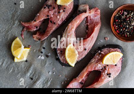 Blick von oben auf frische Forellensteaks, die auf Backpapier angeordnet sind und bereit sind, mit Zitronenscheiben, Salz und Pfeffer in der Nähe einer kleinen Schüssel gemischt fermentiert zu werden Stockfoto