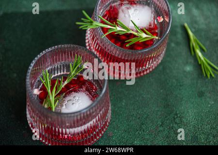 Blick von oben auf zwei Gläser Gin Tonic Cocktail mit Granatapfelkernen und einem Zweig Rosmarin, auf einer dunkelgrünen strukturierten Oberfläche mit einem einzelnen Rosmarin Stockfoto