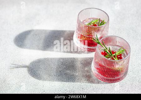 Von oben genießen Sie sonnendurchflutete Gin Tonic-Cocktails mit Granatapfel und Rosmarin in strukturierten Gläsern auf einer hellen Oberfläche Stockfoto