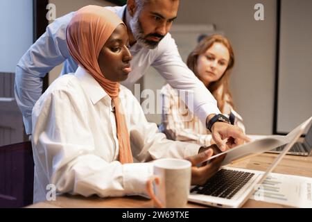 Konzentrierte sich auf verschiedene Kollegen mit Laptop und Dokumenten, die neue Geschäftsstrategie diskutierten, während sie in modernen Büros an Projekten arbeiteten Stockfoto