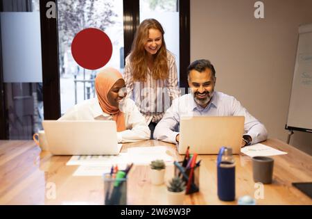 Konzentrierte multiethnische Kollegen in lässiger Kleidung am Tisch mit Laptops und arbeiten an Geschäftsprojekten im modernen Büro Stockfoto