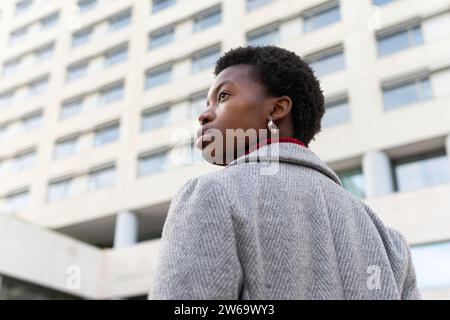 Niedriger Rückblick einer jungen afroamerikanischen Frau, die vor verschwommenen Gebäuden im Hintergrund auf der Straße steht Stockfoto