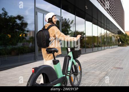 Junger städtischer Pendler mit Helm, der auf einem E-Bike in der Stadt pausiert. Stockfoto