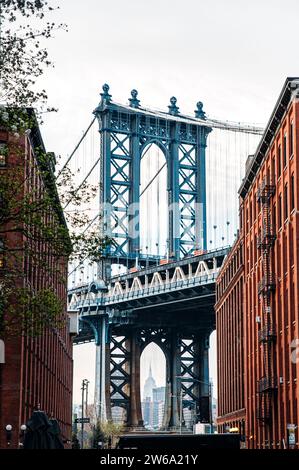 Ein malerischer Blick auf die Manhattan Bridge von einer kopfsteingepflasterten Straße in DUMBO, Brooklyn, mit historischen Gebäuden, die beide Seiten flankieren. Stockfoto