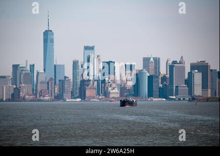 Ein Fernblick auf die Skyline von Manhattan, dominiert vom One World Trade Center, mit einem Schiff, das auf dem Hudson River im Vordergrund segelt. Stockfoto