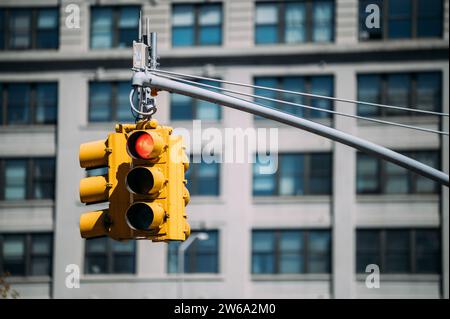 Vor dem Hintergrund der urbanen Architektur in Manhattan, New York, steht eine leuchtende gelbe Ampel. Stockfoto