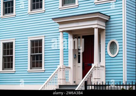 Ein bezauberndes blaues Haus mit weißen Zierleisten und einer lebendigen roten Tür, die traditionelle Architektur zeigt, in Manhattan, New York. Stockfoto