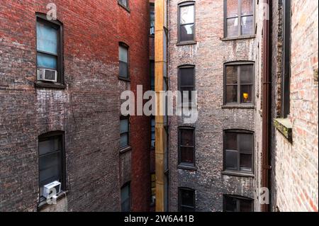 Eine enge Gasse zwischen alten Backsteingebäuden mit mehreren Fenstern und Klimaanlagen in Manhattan, New York. Stockfoto