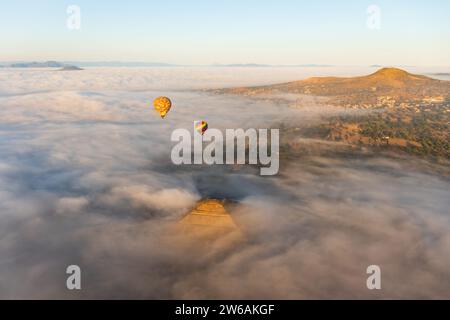 Heißluftballons, die während des Sonnenaufgangs über einer dichten Wolkendecke aufsteigen, mit den goldenen Tönen der Morgensonne auf der Spitze der Pyramide des Stockfoto