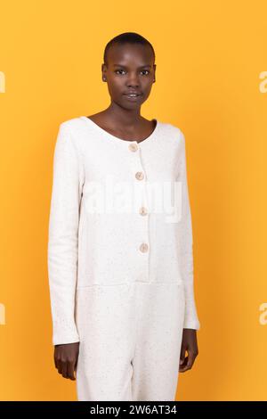 Porträt einer selbstbewussten, ruhigen afroamerikanischen jungen Frau mit kurzen Haaren in weißen Casuals, während sie vor gelbem Hintergrund in die Kamera blickt Stockfoto