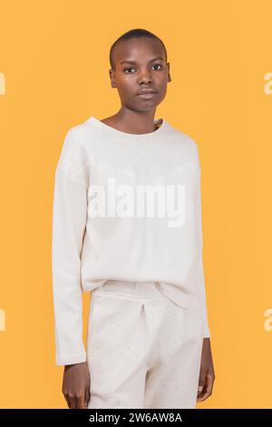 Selbstbewusste, schlanke afroamerikanische junge Frau in modischer Freizeitkleidung, die auf die Kamera blickt, während sie vor gelbem Hintergrund steht Stockfoto