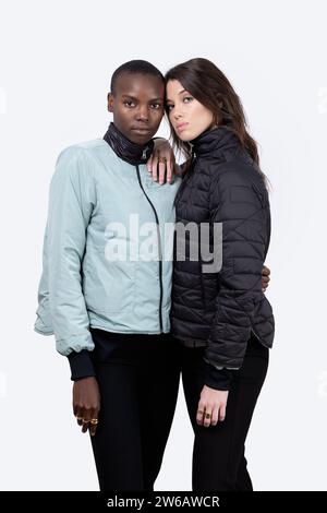 Porträt selbstbewusster, multirassischer weiblicher Freunde, die Winterjacken tragen, während sie vor weißem Hintergrund zusammen stehen Stockfoto