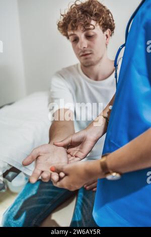 Junge männliche Patientin, die auf dem Bett sitzt und Hand zeigt, um weibliche Ärztin im modernen Krankenhaus zu beschneiden Stockfoto