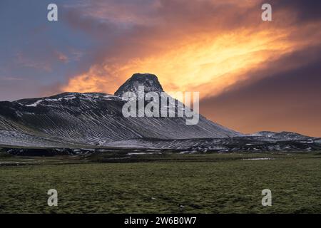 Ein atemberaubender Sonnenuntergang färbt den Himmel mit feurigen Farben hinter einem schneebedeckten Berggipfel in der zerklüfteten Landschaft Islands. Stockfoto