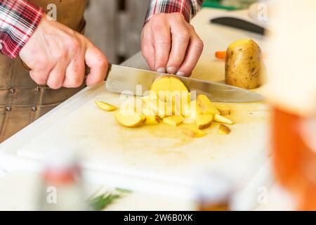 Hoher Handwinkel eines anonymen Küchenchefs, der gelbe Kartoffeln auf einem weißen Schneidebrett in der Küche schneidet Stockfoto