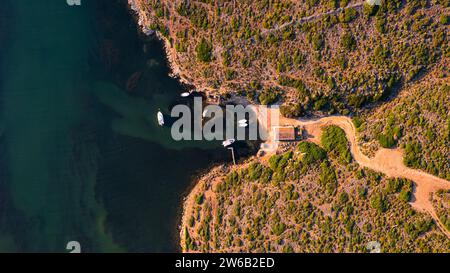 Eine Aufnahme über dem Kopf, die die Kurven einer Küstenstraße erfasst, während sie sich an die Konturen einer dramatischen Klippe schmiegt. Naturhafen Sanitja in Menorca, Spanien Stockfoto