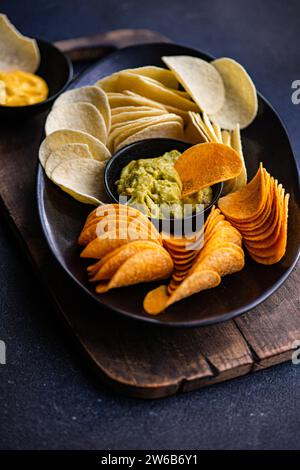 Blick von oben auf einen Teller mit verschiedenen Crisps mit Guacamole und Käsedips auf einem Schneidebrett Stockfoto