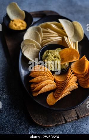 Blick von oben auf einen Teller mit verschiedenen Crisps mit Guacamole und Käsedips auf einem Schneidebrett Stockfoto