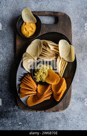 Blick von oben auf einen Teller mit verschiedenen Crisps mit Guacamole und Käsedips auf einem Schneidebrett Stockfoto