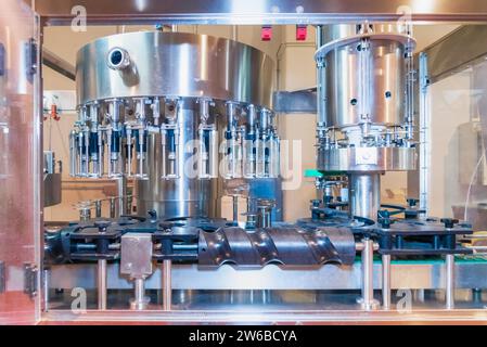 Innenraum einer modernen Fabrik mit automatischer Weinabfüllmaschine, die auf einem Metallständer in einer Industrieanlage platziert wird und Wein eingießt Stockfoto