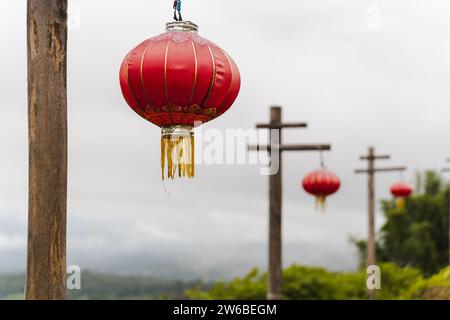 Traditionelle rote chinesische Laternen hängen während der Feiertage an Holzpfählen vor bewölktem Himmel in Thailand Stockfoto