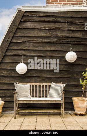 Kleine Sitzbank mit Kissen auf der Dachterrasse des modernen Apartments mit weißen Laternen, die an einer Holzwand hängen Stockfoto